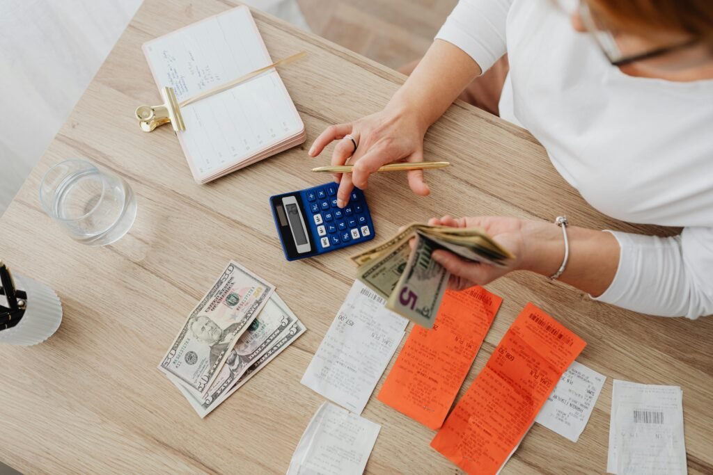 pexels-photo-5900183-5900183 Overhead view of a person using a calculator to manage cash and receipts at a desk.