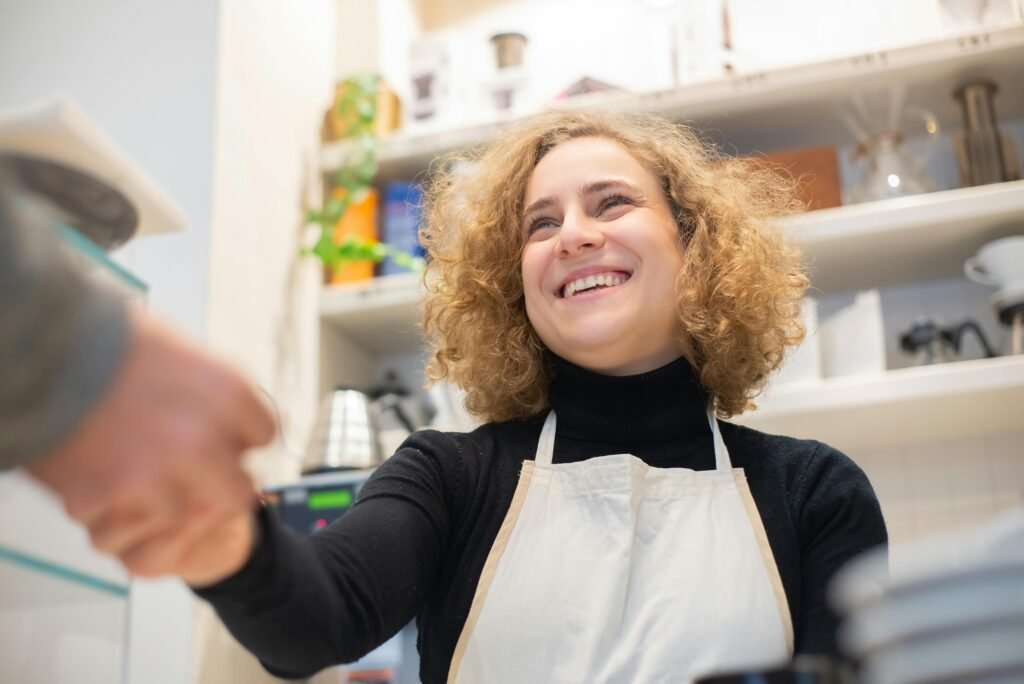 pexels-photo-6684795-6684795 Smiling barista in café, engaging positively with customer, signifying hospitality.