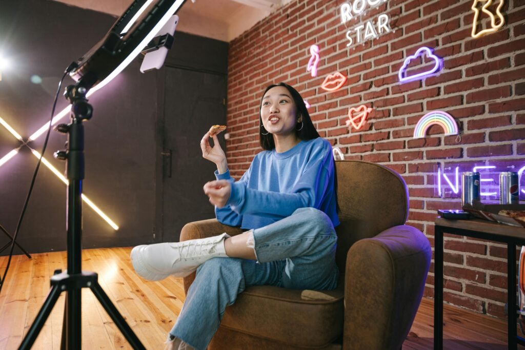 pexels-photo-7676402-7676402 Young Asian woman streaming live indoors with neon lights, engaging audience through technology and creative content.